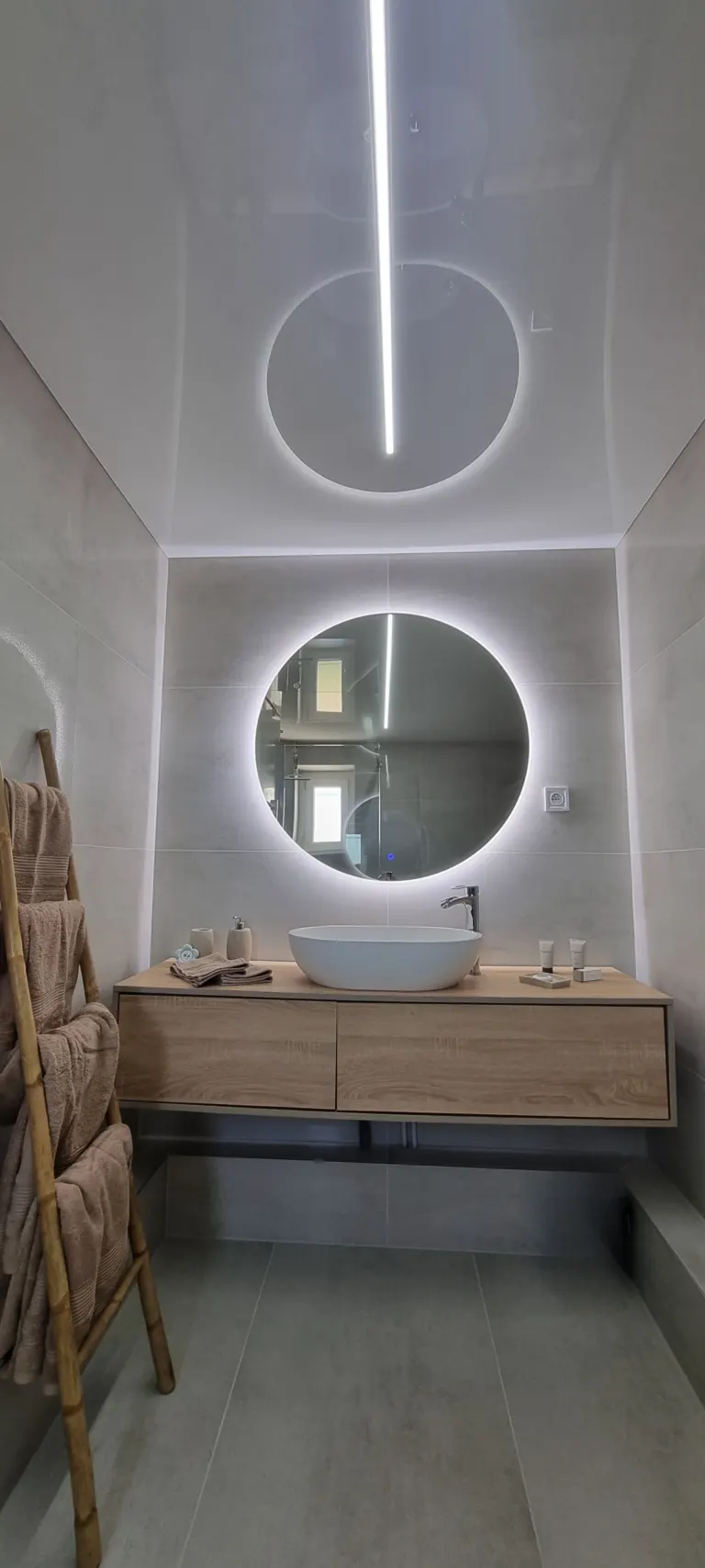 Salle d'eau avec vasque, miroir rond lumineux et échelle porte-serviettes